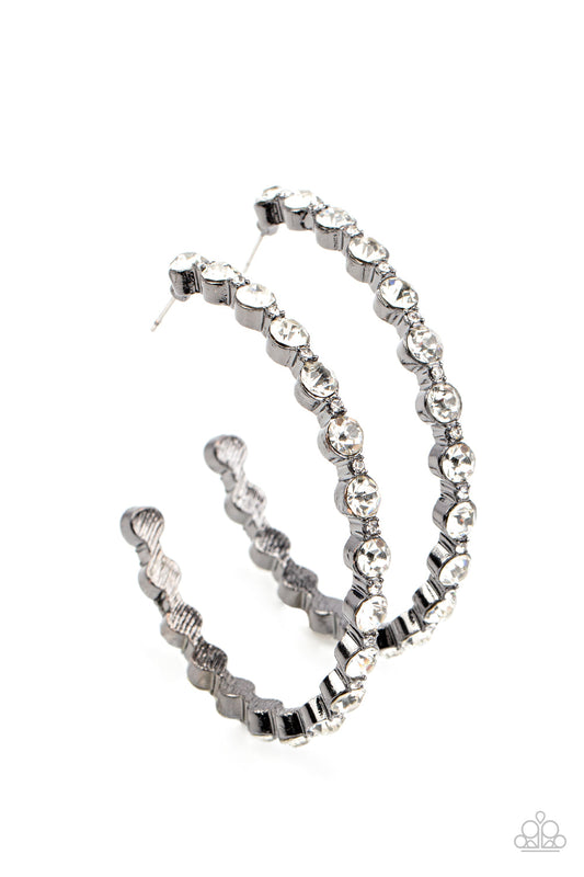 The Paparazzi Jewelry Royal Reveler - Black Earrings! These earrings are sure to add some glamour and sparkle to your look. They're encased in sleek gunmetal fittings and feature a glamorous collection of glittery white rhinestones that delicately coalesce into an oversized hoop for a truly statement-making look. Whether you're dressing up for a formal event or just want to add some extra flair to your everyday style, these earrings are sure to make a big impression.